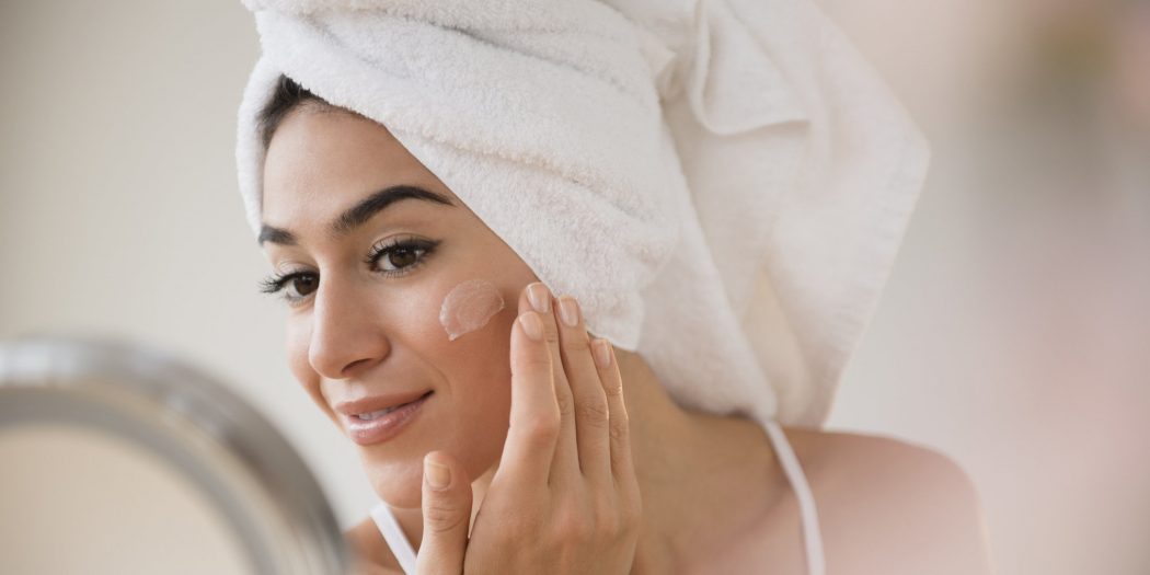 Woman with hair in towel rubbing lotion on face