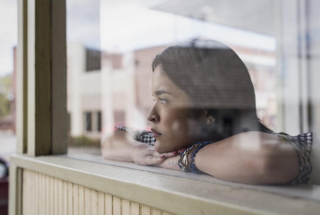 Young hispanic woman gazing out store window in small town
