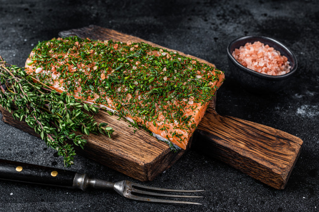 Gravlax cured salmon with dill and salt on wooden board. Black background. Top view