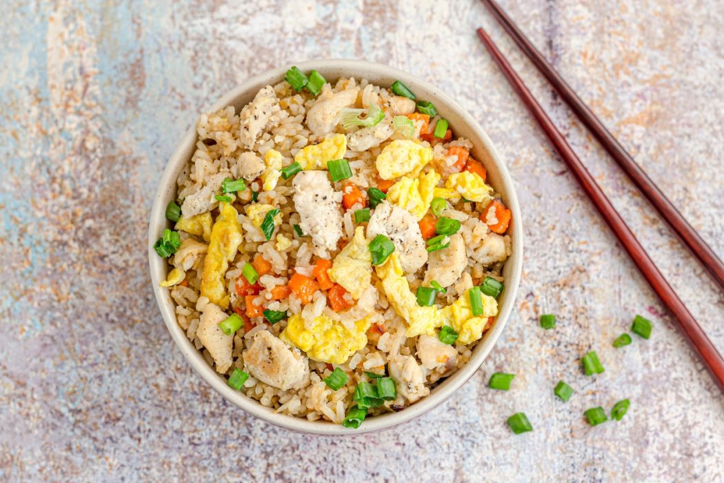 A Bowl of Asian Chicken Fried Rice with Veggies and Scrambled Eggs on Wooden Base with Chopsticks